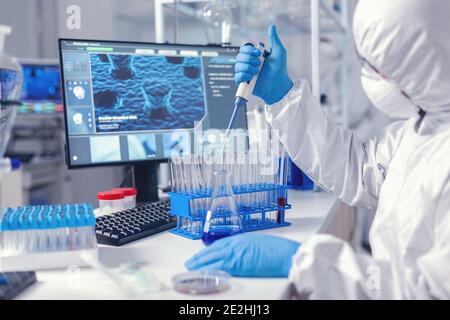 Healthcare researcher in ppe suit working with micro pipette in time of coronavirus. Chemist in modern laboratory doing research using dispenser during global epidemic with covid-19. Stock Photo