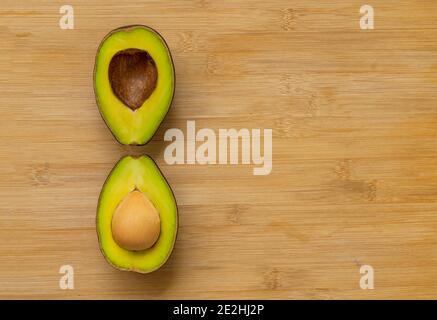 Two cut half avocados with unique arrangement on bamboo cutting board, top view image, space for copy and design. Stock Photo