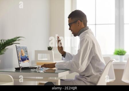 Doctor video calling senior woman and waving hand at laptop screen, greeting her Stock Photo