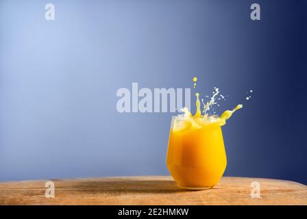 Glass of fresh orange juice splash on on wooden table and blue background. Dynamic pour of fruit juice in the morning. Space for text Stock Photo