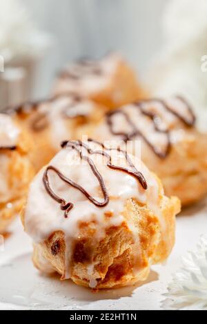 Closeup view of delicious fresh profiteroles filled with custard on white table. Homemade tasty eclairs. Concept of desserts, restaurant food. Stock Photo