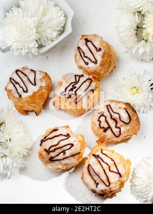 Closeup view of delicious fresh profiteroles filled with custard on white table. Homemade tasty eclairs. Concept of desserts, restaurant food. Stock Photo