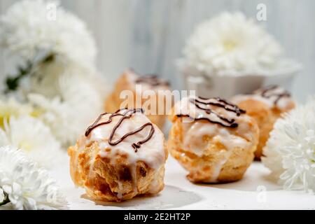 Closeup view of delicious fresh profiteroles filled with custard on white table. Homemade tasty eclairs. Concept of desserts, restaurant food. Stock Photo