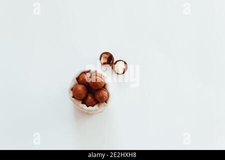 Raw macadamia nuts in canvas bowl on a white solid background. Minimal flat composition Stock Photo