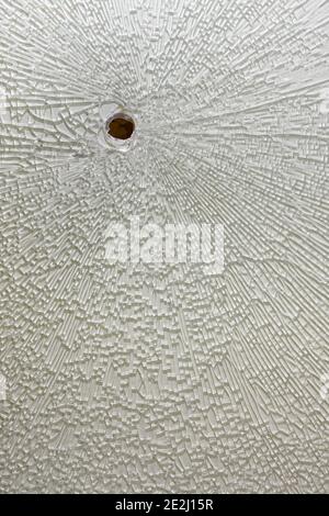 Broken tempered glass with white backing, cracks around the hole Stock Photo
