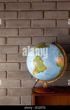 Globe on top of vintage bookcase in front of brick wall Stock Photo