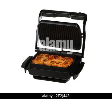 Homemade pizza with salami, bacon, tomato sauce, yellow cheese and mozzarella in a black electric grill in a baking dish with a non-stick coating isol Stock Photo