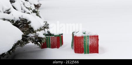 Two large red Christmas decoration gifts outside covered in snow after a storm next to a bush Stock Photo