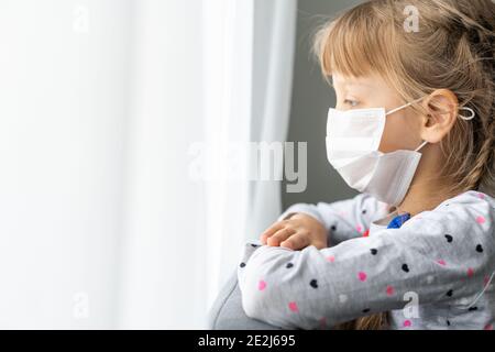 Caucasian sick little girl in medical mask during coronavirus epidemic prays Stock Photo
