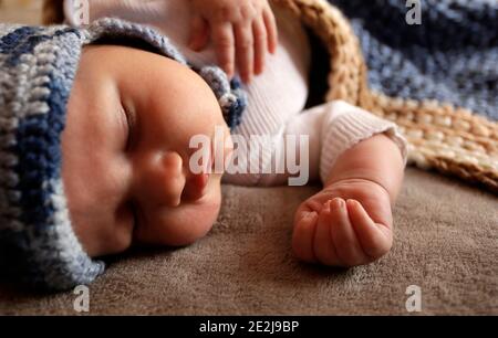 Sweet newborn baby boy with chubby cheeks sleep in bed covered by plaid in warm blue knitted hat during day Stock Photo