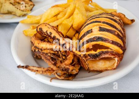 Grilled squid served with vegetables and fries. Traditional Greek dish. Stock Photo