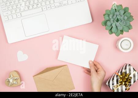 Womans hands holding craft envelope with copyspace on pink pastel table top view. Flat lay composition for Valentines day. Happy womans day  Stock Photo