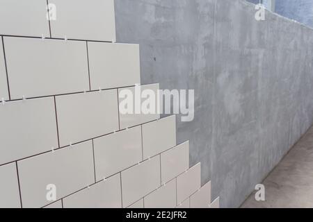 Laying Ceramic Tiles on the wall. White ceramic tiles. Renovation work. Ceramic white tiles on wall, renovation concept. Stock Photo
