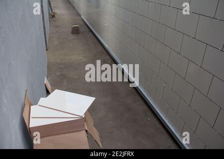 Laying Ceramic Tiles on the wall. White ceramic tiles. Renovation work. Material for repairing walls in a building. Stock Photo