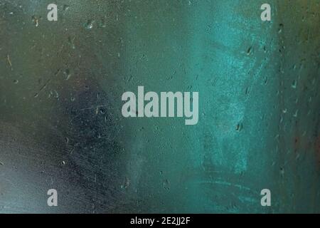 Wet steamy window inside bus on a rainy day, blurred orange and blue