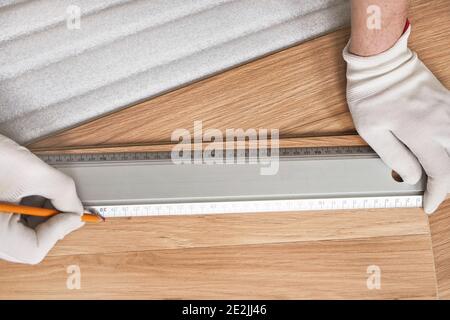 Installing laminated floor, detail on man hands in white gloves making mark with pencil using aluminium ruler Stock Photo