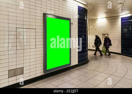 Advertising board display green mockup on wall with white tiles at underground station passage, blurred people in background Stock Photo