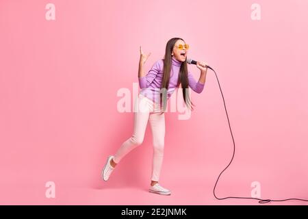 Full size photo of crazy little kid girl sing song in mic show horned sign isolated over pastel color background Stock Photo