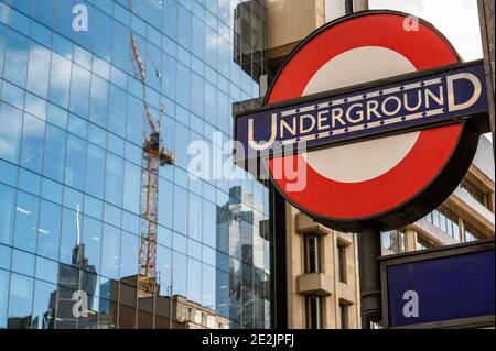 London Underground Tube Station sign with a construction crane and city buildings reflected in a modern glass office building in the background. Stock Photo