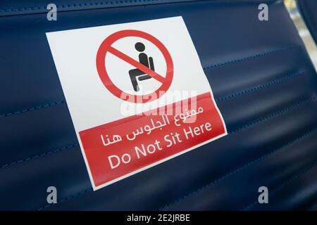 Sticker sign 'Do not sit here' in english and arabic on a seat at the airport, travel during coronavirus pandemic, social distancing in the terminal.