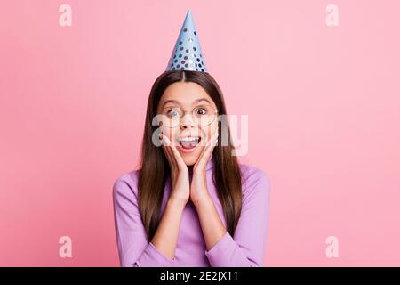 Photo of astonished little kid girl in birthday cap touch hands cheeks wear violet jumper isolated on pastel color background Stock Photo