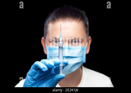 doctor in protective mask and sterile gloves holds syringe with vaccine for injection against virus in his hands and looks carefully assesses medical Stock Photo