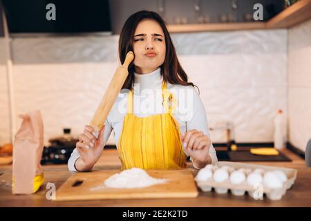 Young housewife is wondering and thinking about something. Pretty woman has difficulties while cooking in the kitchen . Stock Photo