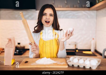 Happy attractive young adult woman lady housewife baker wear apron holding pin rolling dough on kitchen Stock Photo