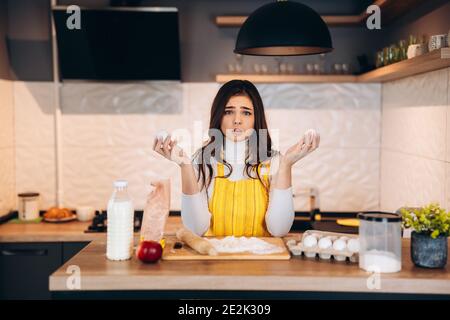 Young housewife is wondering and thinking about something. Pretty woman has difficulties while cooking in the kitchen . Stock Photo