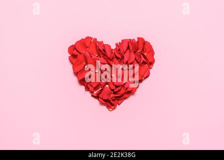 Valentine day heart made of rose petals, isolated on pink background. Flat lay with a romantic red heart. Red roses petals in a heart shaped layout. Stock Photo