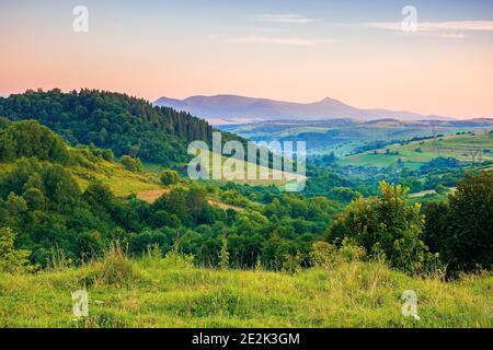 mountainous rural landscape at dawn. beautiful scenery with forests, hills and meadows in morning light. ridge with high peak in the distance. village Stock Photo