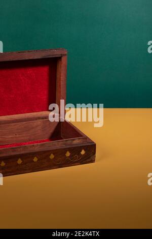 An old vintage handcarved wooden box in a dark brown color and golden details opened up on a yellow surface with a green background. An antique authen Stock Photo