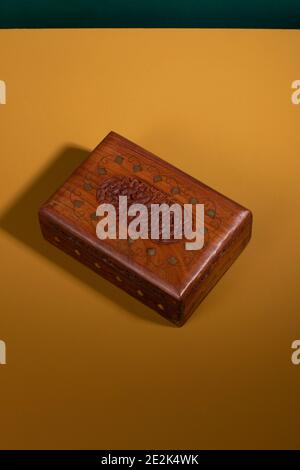 Vintage old handcarved wooden box in a dark brown color with golden details on a yellow surface with a green background. An antique authentic handmade Stock Photo