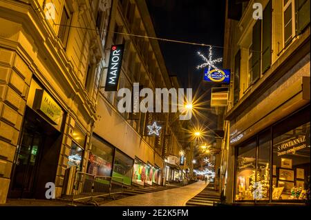 Lausanne, Vaud, Switzerland - 01.10.2021: Night illuminated scenery of street and road with decorated Christmas light with Manor store. Stock Photo