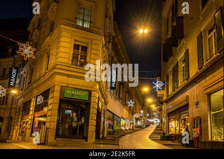 Lausanne, Vaud, Switzerland - 01.10.2021: Night illuminated scenery of street and road with decorated Christmas light with Manor store. Stock Photo