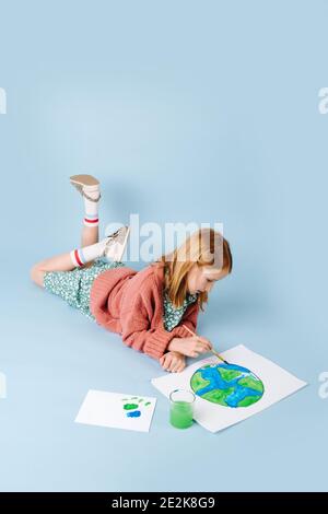 Red-haired girl lying on the floor draws a green-blue planet Stock Photo