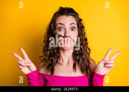 Photo portrait of girl holding two v-signs making fake mustache pouting wearing pink crop-top isolated on bright yellow colored background Stock Photo