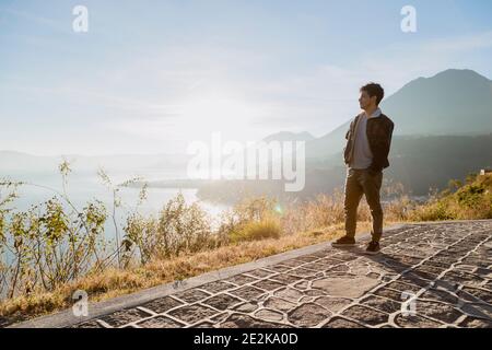 Young traveler on top of the mountain watching the sunrise at Lake Atitlán - Hispanic young man enjoying the sunrise with volcanoes and mountains land Stock Photo