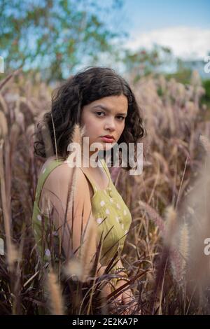 beautiful girl crouching in the flowers with serious face and with a trees behind her Stock Photo