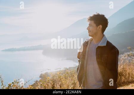 Young traveler on top of the mountain watching the sunrise at Lake Atitlán - Hispanic young man enjoying the sunrise with volcanoes and mountains land Stock Photo