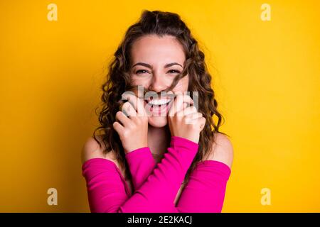 Photo portrait of silly brunette girl making hair mustache laughing holding with two hands wearing fuchsia crop-top isolated on vivid yellow colored Stock Photo