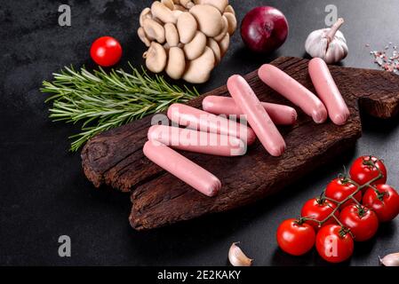 Boiled sausages on a wooden cutting board on a dark concrete background. Unhealthy food Stock Photo