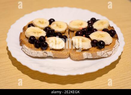 A healthy dessert for breakfast, lunch or dinner dark bread with peanut butter, black currant and banana slices Stock Photo