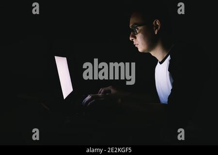 Caucasian workaholic young man working late night from home sitting on a desktop and using his laptop Stock Photo
