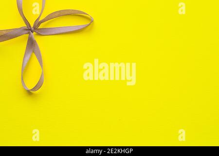 Yellow bright background with a gray ribbon bow in the upper left corner. Holiday concept. Stock Photo