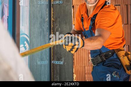 Construction Worker with Measuring Tape in His Hands Taking Sizes Inside Newly Built Building. Construction Industry Theme. Stock Photo