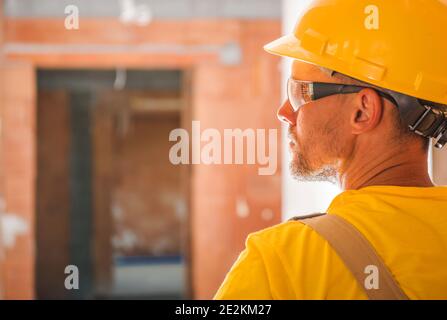Yellow Uniform and Hard Hat Wearing Construction Worker Inside Newly Built Concrete Brick Commercial Building Rear Head Close Up. Construction Profess Stock Photo