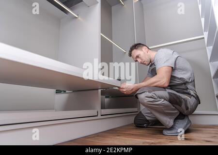Caucasian Men in His 40s Assembling Elegant Modern White Closet Furnitures Inside His Apartment. Stock Photo