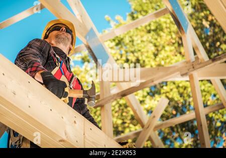 Caucasian Construction Worker in His 40s Between Wooden Roof Elements of the House Skeleton Frame. Construction Industry Theme. Stock Photo