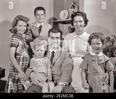 1950s SMILING FAMILY PORTRAIT WOMAN MOTHER MAN FATHER FOUR CHILDREN TWO BOYS BROTHERS TWO GIRLS SISTERS ALL LOOKING AT CAMERA  - j6877 HAR001 HARS NOSTALGIC PAIR 4 SUBURBAN MOTHERS OLD TIME SURPRISE NOSTALGIA BROTHER OLD FASHION SISTER 1 JUVENILE STYLE WELCOME SONS PLEASED FAMILIES JOY LIFESTYLE SATISFACTION FEMALES MARRIED BROTHERS SPOUSE HUSBANDS HEALTHINESS HOME LIFE 6 COPY SPACE FRIENDSHIP HALF-LENGTH LADIES DAUGHTERS PERSONS MALES SIX SIBLINGS SISTERS FATHERS B&W PARTNER EYE CONTACT DRESSES SUIT AND TIE HAPPINESS CHEERFUL DADS PRIDE SIBLING SMILES CONNECTION JOYFUL STYLISH BABY BOY Stock Photo